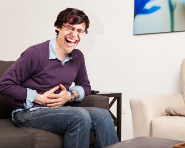 laughing man Profile view of a guy touching his belly and having a stomach ache at home