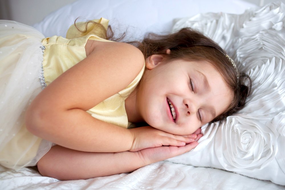 Happy smiling kid sleeping and smiling in her sleep. Dream the little princess on a white bed close-up speaking in dream.