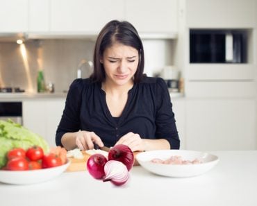 Young housewife cutting onion & crying