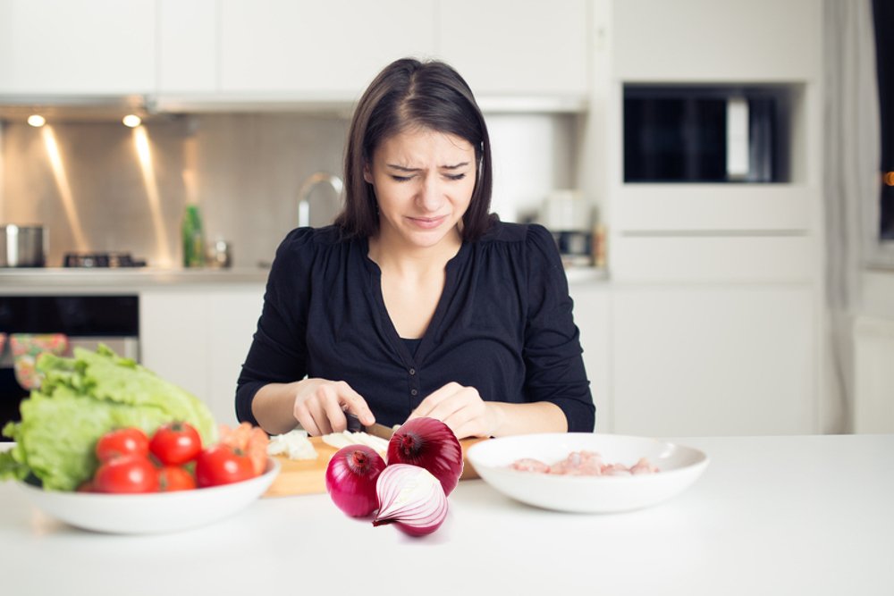 Young housewife cutting onion & crying