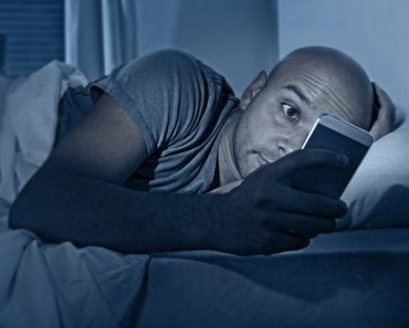 internet addict man awake at night in bed with mobile phone