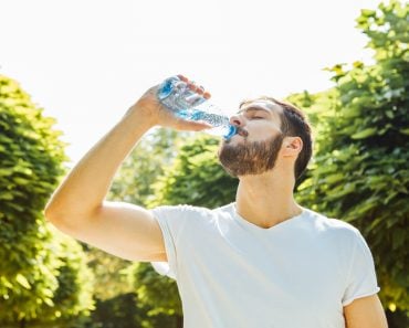 Close up of a man drinking water from a bottle outside