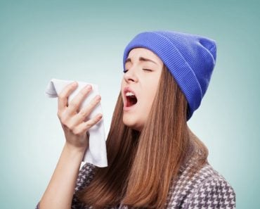 Sick young woman with a flu, sneezing closeup over grey