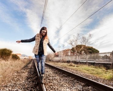 Beautiful Young Woman Walking in Balance on Railway Tracks. The Railroad is in a Residential Area. The Girl has a Casual Look.