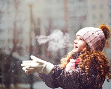 Cute little girl stretches her hand to catch falling snowflakes. First snow. Toning instagram filter.