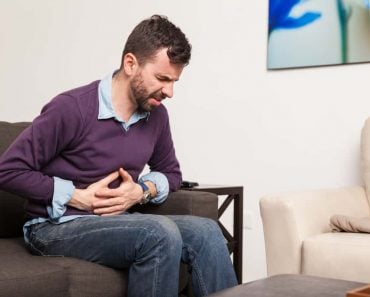 Profile view of a guy touching his belly and having a stomach ache at home