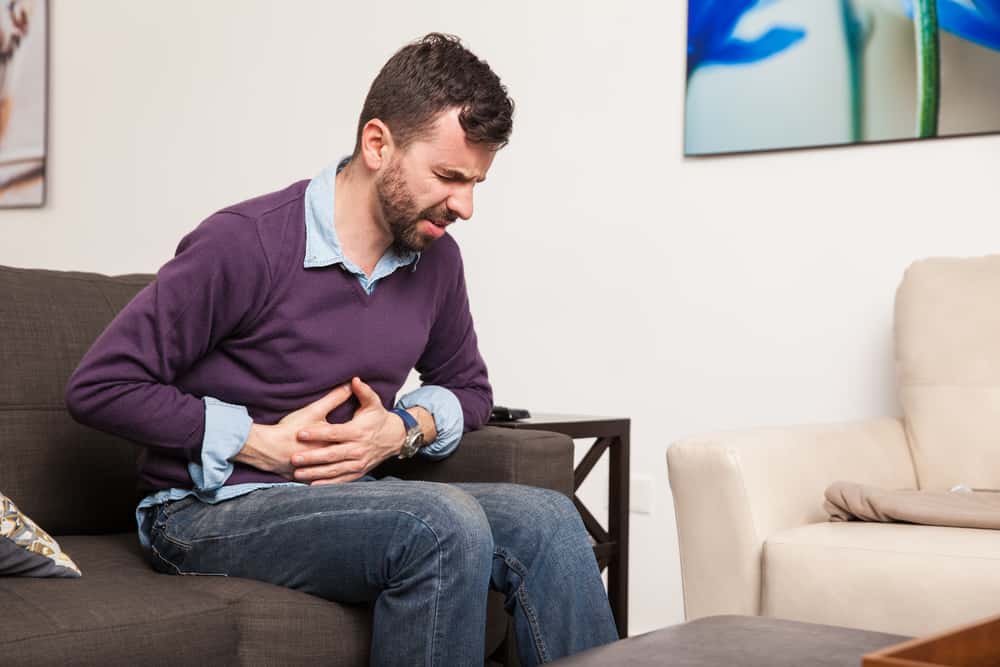 Profile view of a guy touching his belly and having a stomach ache at home