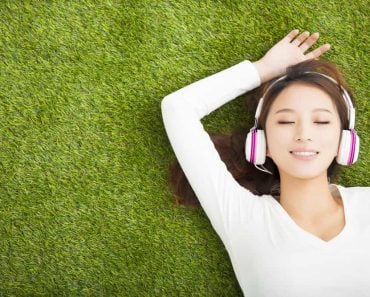 Relaxed woman listening to the music with headphones lying on the grass