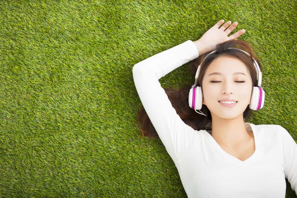 Relaxed woman listening to the music with headphones lying on the grass