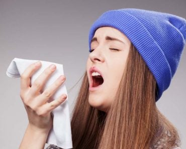 Sick young woman with a flu, sneezing closeup over grey