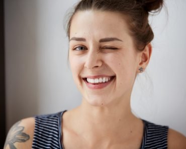 Portrait of attractive cute woman winking over gray background. Looking at the camera. Positive human emotion facial expression body language. Funny girl ( WAYHOME studio)(s)