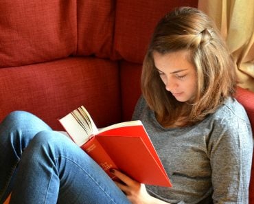 Young girl reading orange cover book on sofa