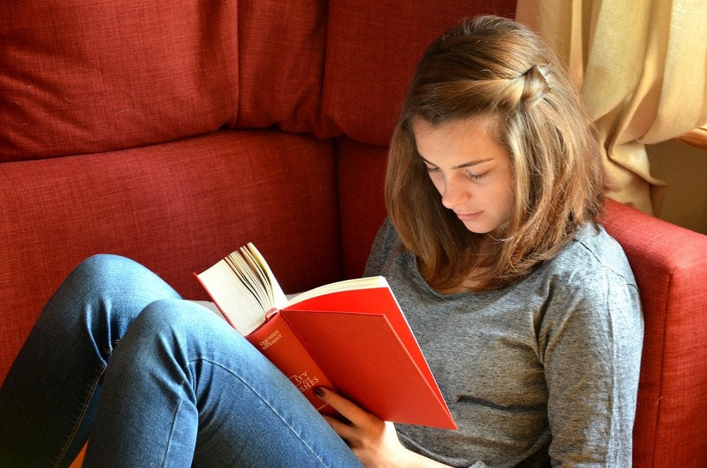 Young girl reading orange cover book on sofa