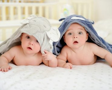 Adorable five months old baby boy twins in character towels after taking a bath or shower, in bed at home. Nursery for children. Tummy time activities for infants - Image( Zoia Kostina)s