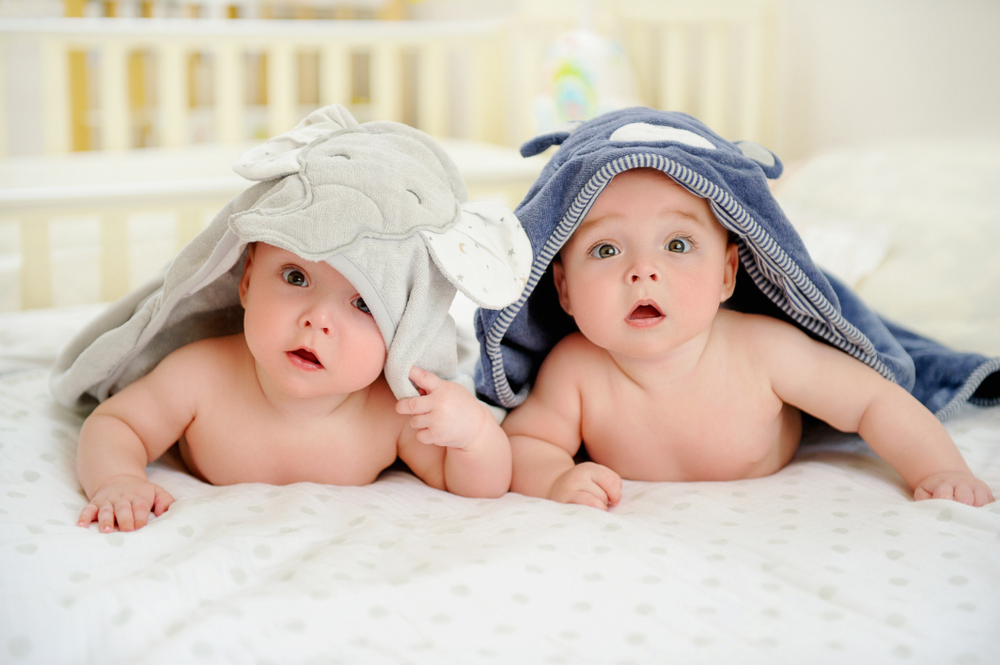 Adorable five months old baby boy twins in character towels after taking a bath or shower, in bed at home. Nursery for children. Tummy time activities for infants - Image( Zoia Kostina)s