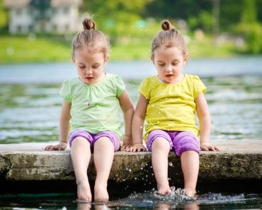 Identical twins girls are exercising on lake shore, sprinkling water. Children sitting on lake side, playing with water. Healthy and active children lifestyle. - Image(JGA)s