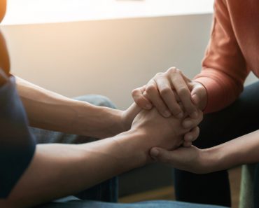 PTSD Mental health concept, Psychologist sitting and touch hand young depressed asian man for encouragement near window with low light environment.Selective focus. - Image( Chanintorn.v)s