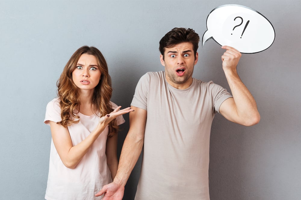 Portrait of a young frustrated couple having an argument while standing and holding speech bubble isolated over gray wall - Image(Dean Drobot)s