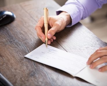 Close-up Of A Businessperson's Hand Signing Cheque In Office - Image( Andrey_Popov)S