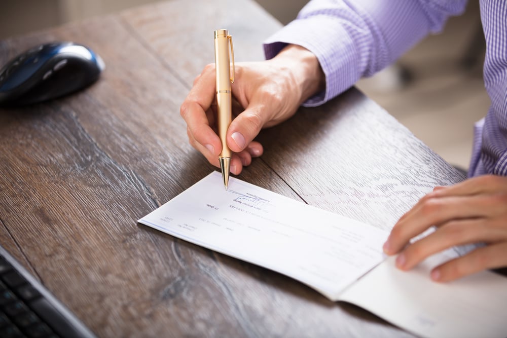 Close-up Of A Businessperson's Hand Signing Cheque In Office - Image( Andrey_Popov)S