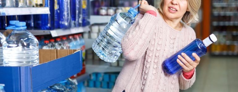 Tense modern woman lifting heavy bottle of still water while shopping at grocery store - Image( Iakov Filimonov)s