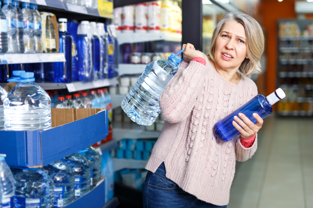 Tense modern woman lifting heavy bottle of still water while shopping at grocery store - Image( Iakov Filimonov)s