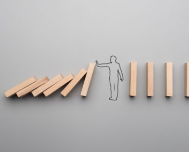 Wide cropped image of the outline of a businessman stopping the domino effect on gray background. - Image(Gajus)s