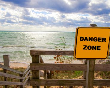 Rip Current Warning. Sign at beach entrance warning of dangerous rip currents as waves crash on to the coast of Lake Michigan. - Image(ehrlif)s