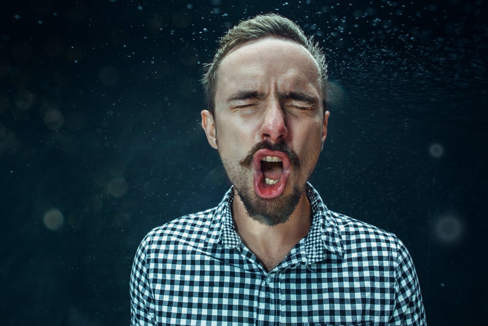 Young funny handsome man with beard and mustache sneezing with spray and small drops, studio portrait on black background(Master1305)s