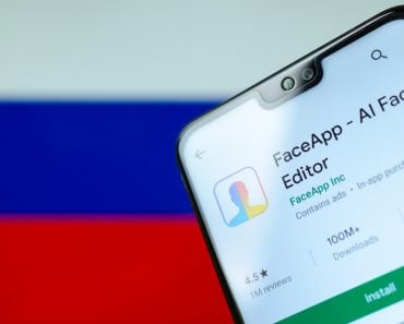 FaceApp logo on the screen of smartphone with the flag of Russia at the blurred background behind it(Ascannio)S