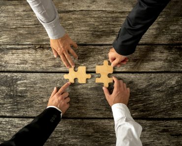 Four successful business men joining two puzzle pieces each being held by two partners(Gajus)s