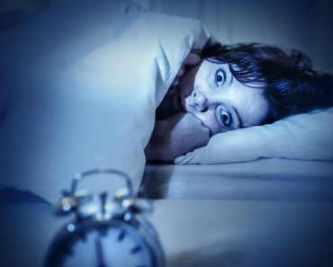 young woman in bed with alarm clock and eyes opened suffering insomnia( Marcos Mesa Sam Wordley)s