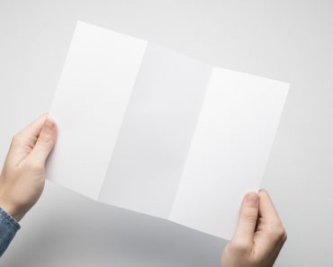 Man in blue shirt is holding a DL Z-Fold white paper flyer(SQS)s