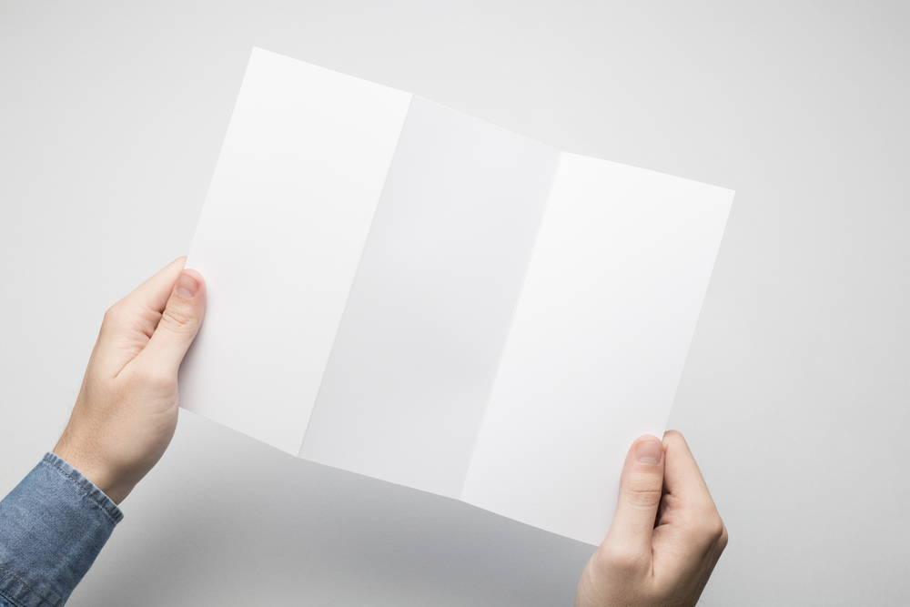 Man in blue shirt is holding a DL Z-Fold white paper flyer(SQS)s