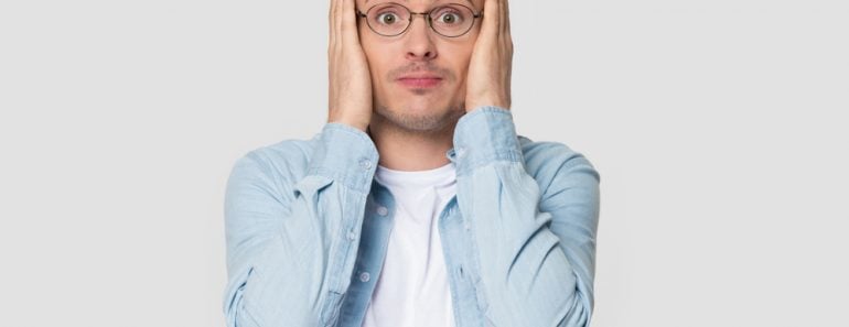 Funny worried man in glasses jean shirt hold head in hands looks concerned pose studio grey wall(fizkes)S