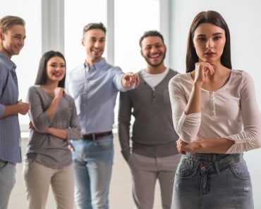 Sad girl in the foreground, young people are pointing and laughing at her in the background(VGstockstudio)S