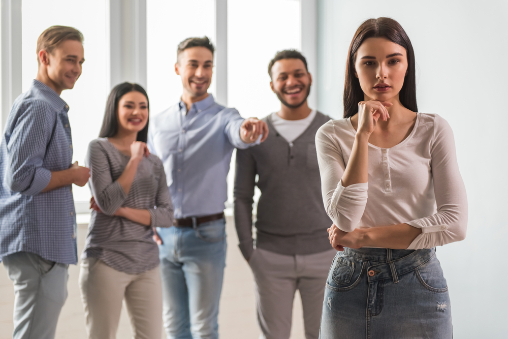 Sad girl in the foreground, young people are pointing and laughing at her in the background(VGstockstudio)S