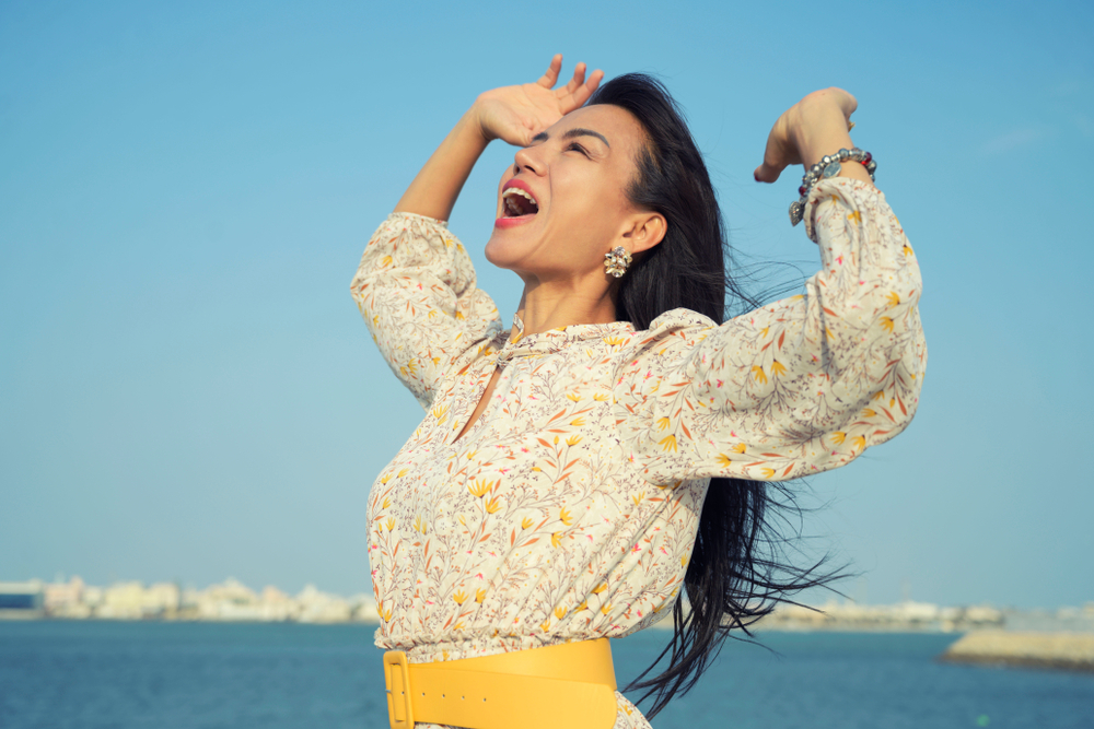 Beautiful Asain woman yelling to sky with hands open in the air over blue sea(Jantira Namwong)s