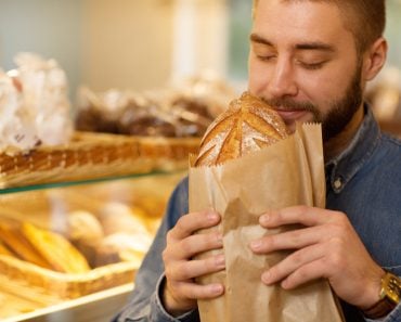 Close up of a young bearded man smelling delicious freshly baked bread at the bakery store(Zoriana Zaitseva)S