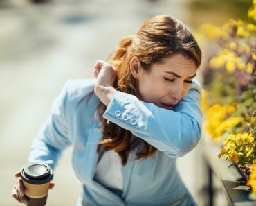 A young businesswoman on a coffee break outside is sneezing into the elbow by an allergy or a cold(MilanMarkovic78)s