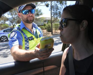 Australian traffic police officer using breathalyzer on woman driver during field sobriety testing(ChameleonsEye)s