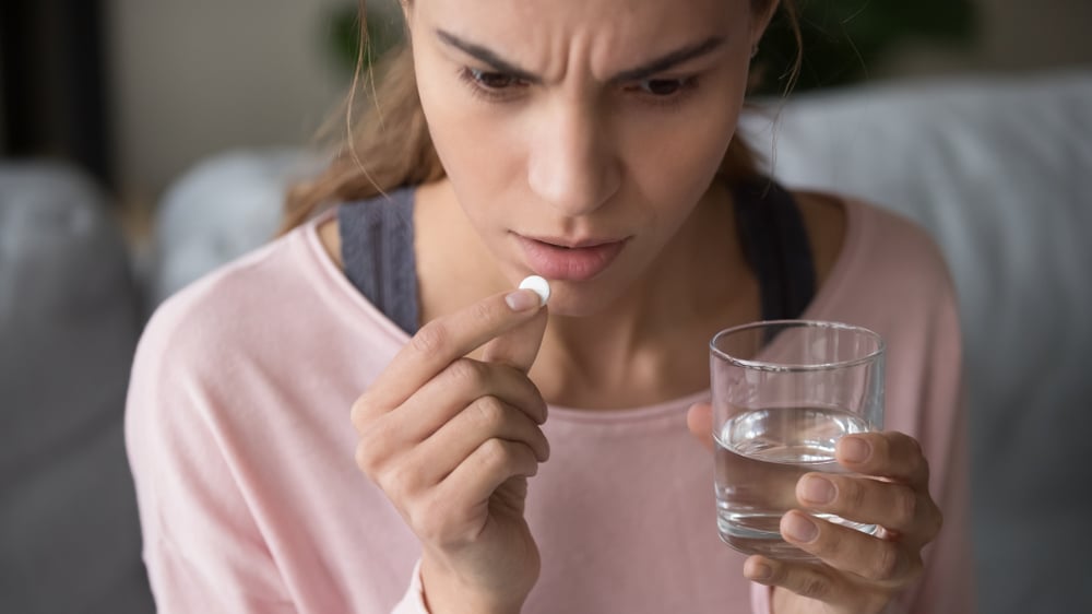 Serious stressed sick millennial mixed race woman holding and thinking over taking round white pill and glass of water(fizkes)s