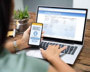 Woman Using Mobile Phone App To Authenthificate Bank Transfer On Laptop(Andrey_Popov)s