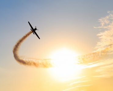 Silhouette,Of,An,Airplane,Performing,Acrobatic,Flight,At,Sundown.,Trace