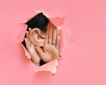 Female,Ear,And,Hands,Close-up.,Copy,Space.,Torn,Paper,,Pink