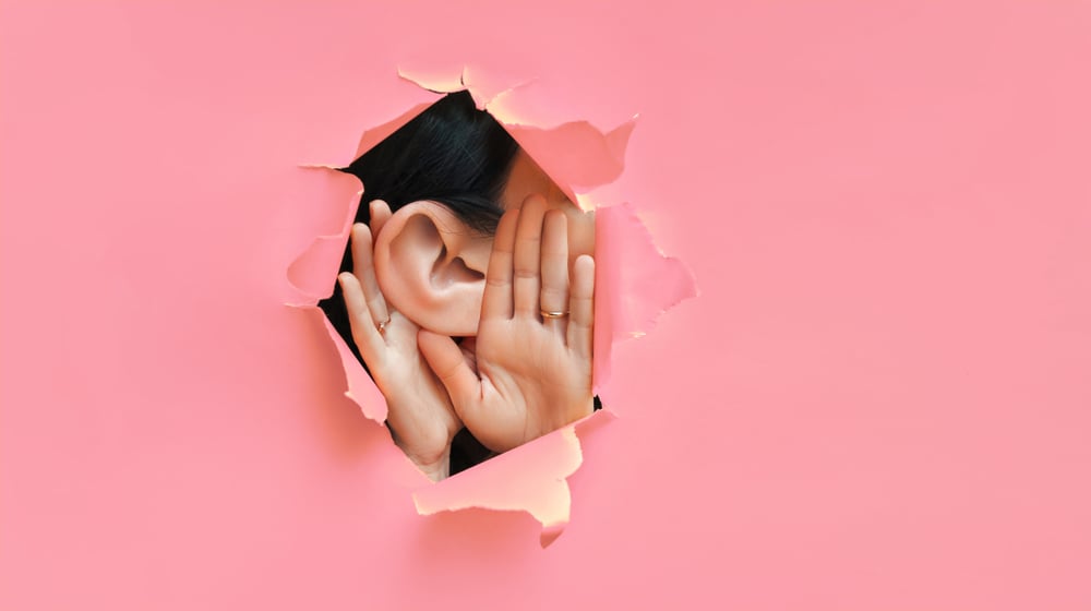 Female,Ear,And,Hands,Close-up.,Copy,Space.,Torn,Paper,,Pink