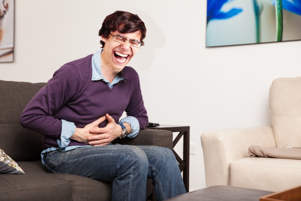 laughing man Profile view of a guy touching his belly and having a stomach ache at home