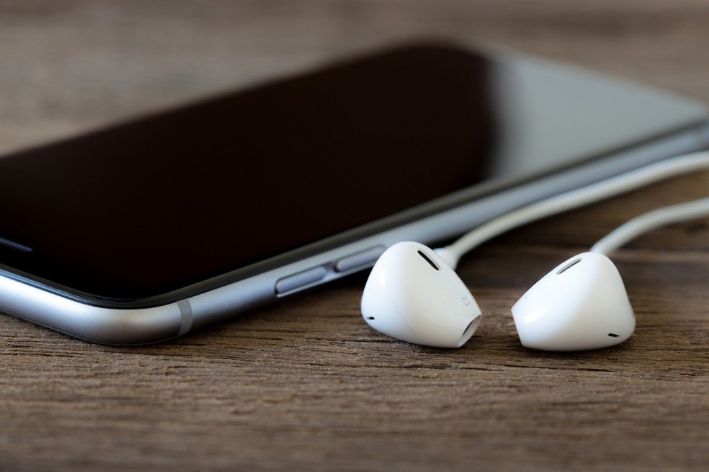 closeup phone and earbud on wood desk