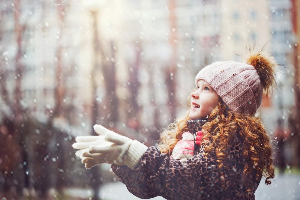 Cute little girl stretches her hand to catch falling snowflakes. First snow. Toning instagram filter.