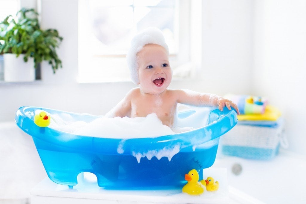 Happy laughing baby taking a bath playing with foam bubbles.